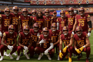 Washington Commanders players posing together on the field in burgundy and gold uniforms before an NFL game at FedExField.